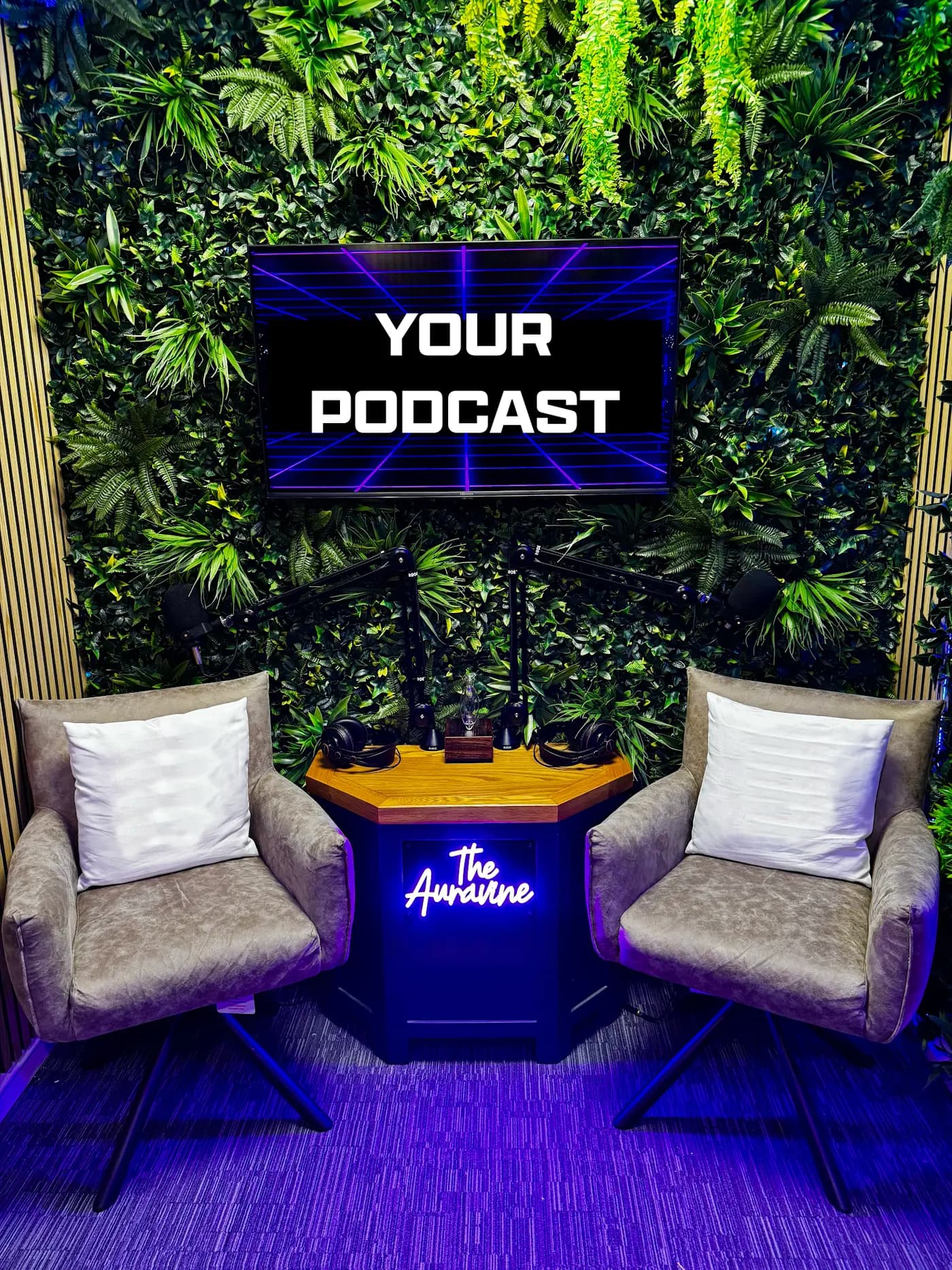 The Auravine podcast studio in Chatham, Kent — two microphones on boom arms over a lit desk, a wall-mounted screen and a living plant wall under purple studio lighting